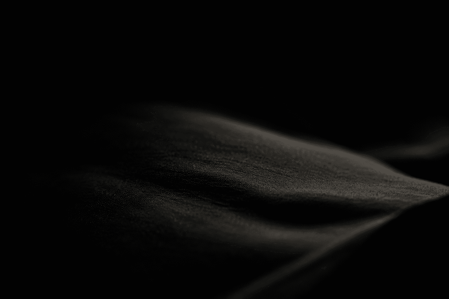 Close-up of dark, softly draped fabric with a single fold catching the light
